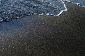 Black volcanic magnetic sand on the seashore.