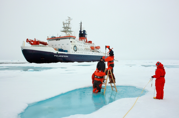 Wissenschaftler messen die Dicke des Meereises mit Eisbohrern, im Hintergrund die Polarstern