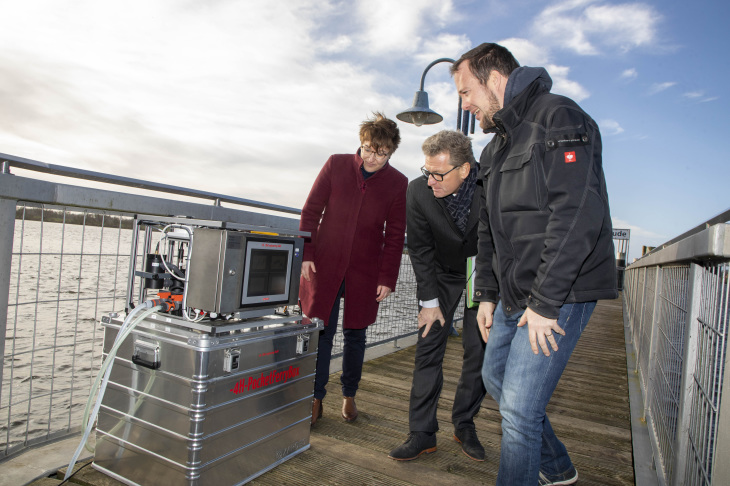 HZG-Wissenschaftler Hendrik Rust (rechts) erläutert die Funktionsweise einer FerryBox, die laufend Messdaten sammelt. Links im Bild: Sina Bold, Projektkoordinatorin, Mitte: der schleswig-holsteinische Wirtschaftsminister Bernd Buchholz. 